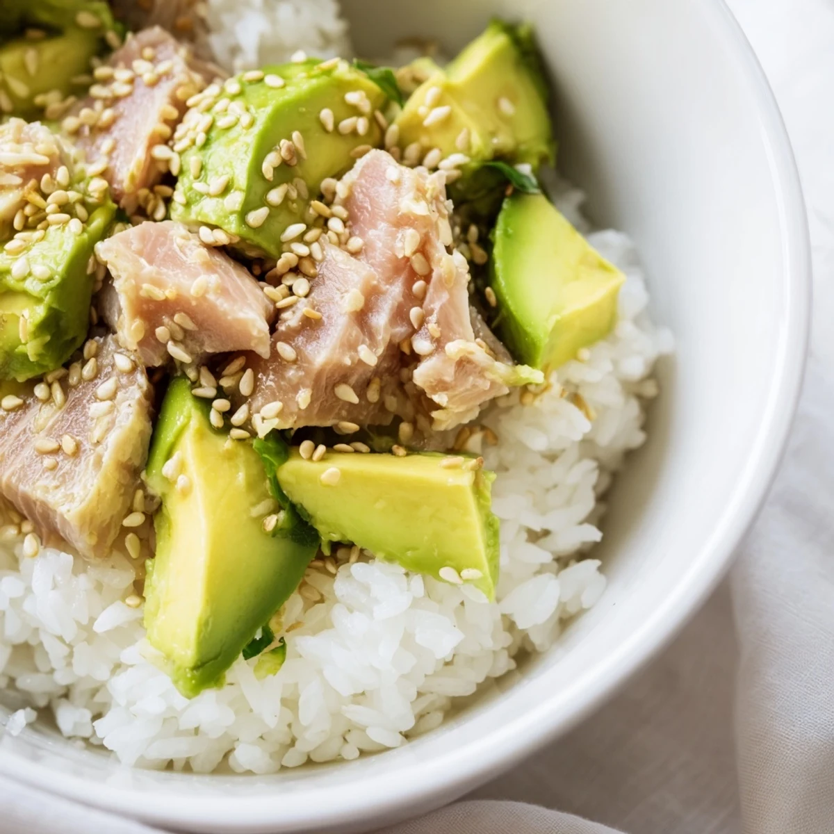 A nourishing tuna avocado rice bowl for two, featuring golden sesame seeds, fresh cilantro, and crisp cucumber over fragrant jasmine rice.