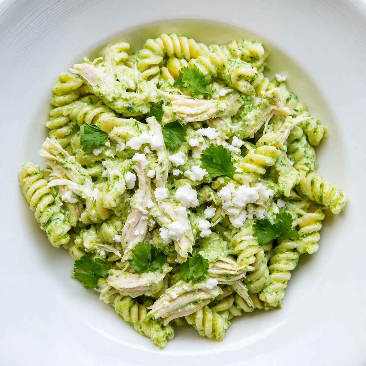 Creamy cilantro lime chicken pasta in a white bowl, rotini coated in vibrant green yogurt sauce garnished with crumbled cotija.