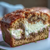 Whole loaf of Cream Cheese Cinnamon Swirl Banana Bread on a rustic wooden board with sliced bananas nearby.