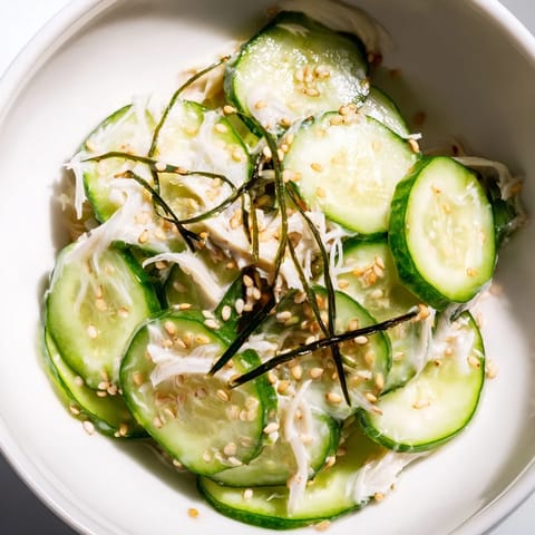Chilled Japanese-American California Roll Cucumber Salad in a white bowl, garnished with sesame seeds, nori, and pickled ginger, served as a refreshing side dish. 