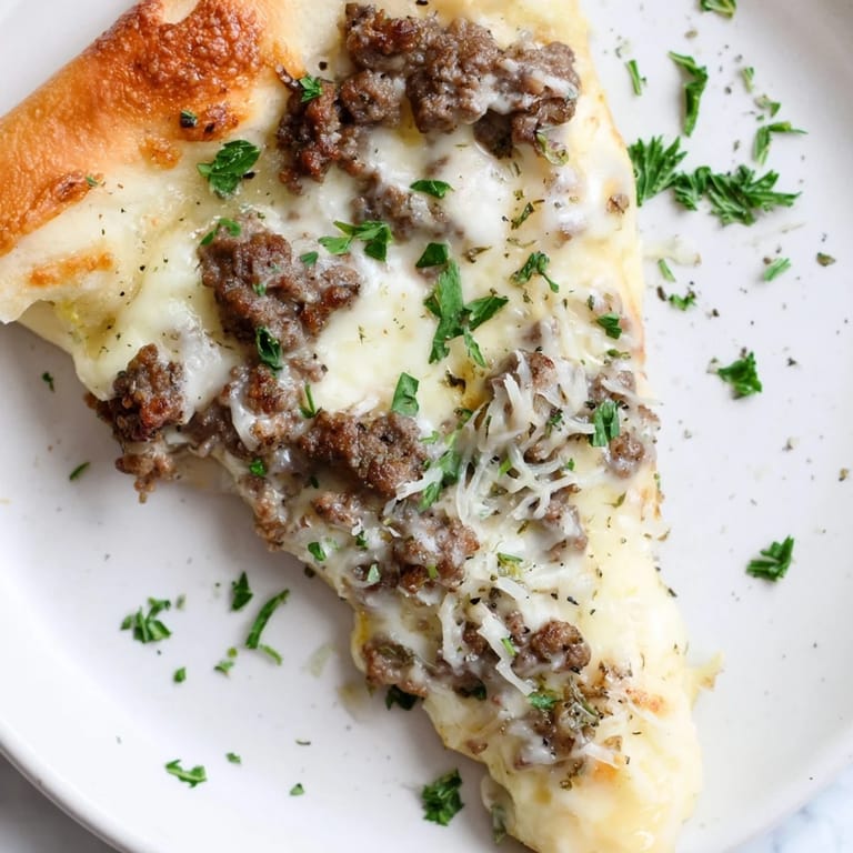 View a close-up of a bubbling Ground Beef Alfredo Pizza, showcasing its creamy Alfredo sauce and browned crust.