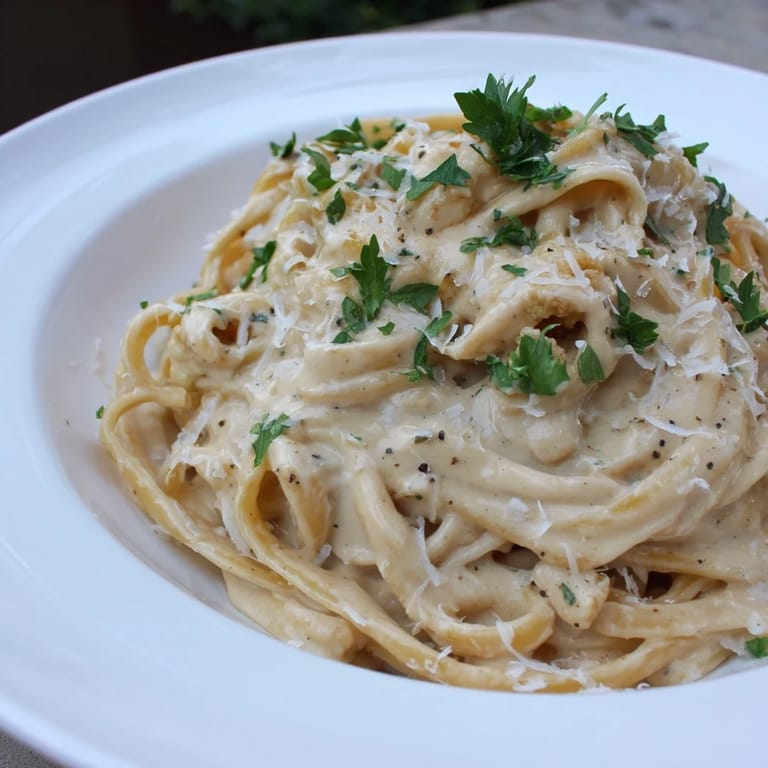 A creamy Roasted Cauliflower Alfredo sauce coats fettuccine in a warm skillet, topped with fresh parsley. 