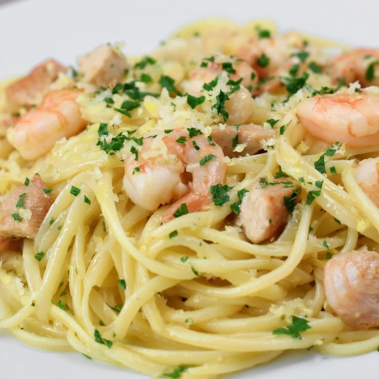 Steam rises from warm Lemon Garlic Shrimp & Chicken Pasta, with bright lemon zest and parsley flecking the al dente noodles and tender proteins.