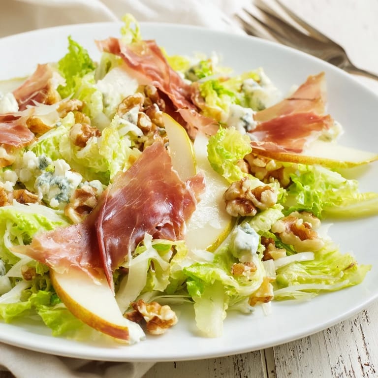 A close-up of frisée, juicy pear slices, and crispy prosciutto with toasted nuts in a light vinaigrette.