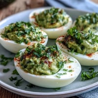 Fresh avocado deviled eggs with vibrant green filling, garnished with herbs and paprika, perfect for spring parties and healthy appetizers.